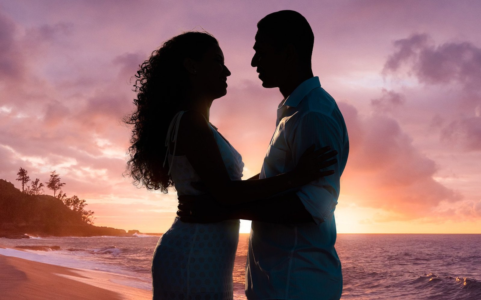 A couple embracing on a beach at sunset, silhouetted against the sea and sky